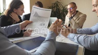 一群年轻的商人坐在现代办公室的桌子旁，正在做一个新的项目。同事认真复习